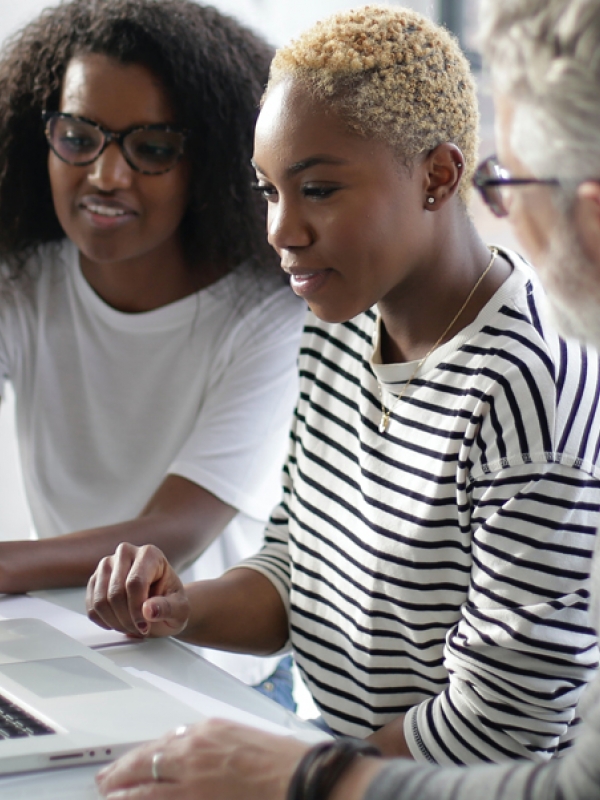 Two women and a man working together in front of a laptop 